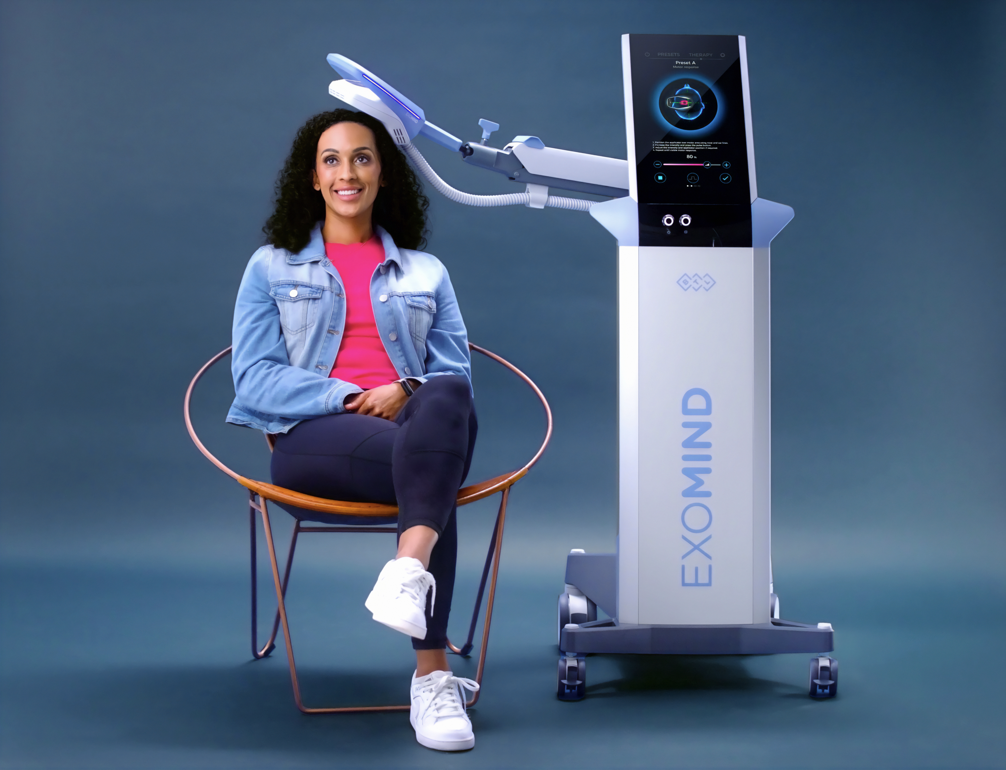 Woman seated beside the Exomind TMS therapy device